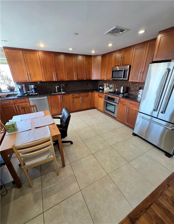 1927 78th St Unit 4A, Brooklyn, NY 11214 - kitchen with appliances with stainless steel finishes, brown cabinetry, backsplash, light tile patterned flooring, and recessed lighting