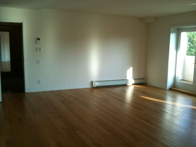 empty room with a baseboard heating unit, wood finished floors, and baseboards