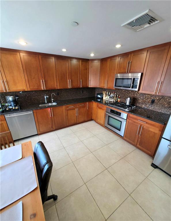 1927 78th St Unit 4A, Brooklyn, NY 11214 - kitchen featuring appliances with stainless steel finishes, backsplash, brown cabinets, light tile patterned floors, and recessed lighting