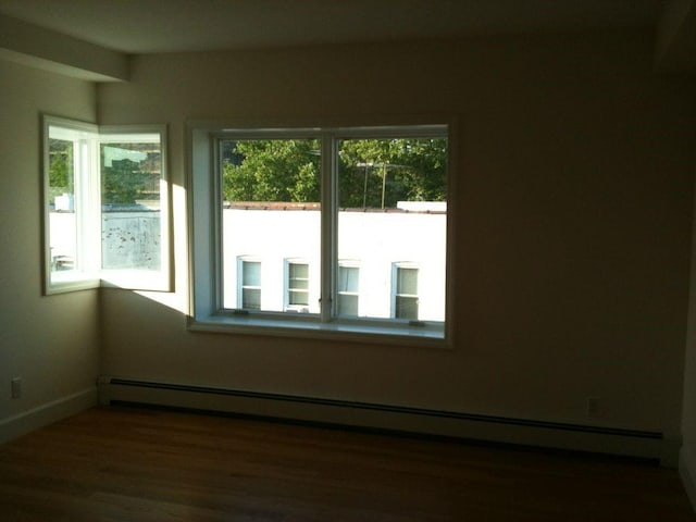 unfurnished room featuring a baseboard heating unit and dark hardwood / wood-style floors