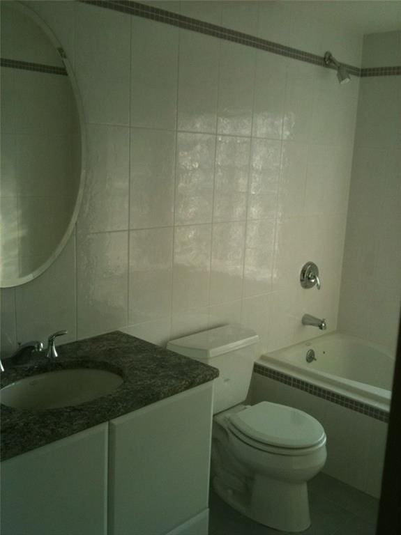 bathroom featuring toilet, tiled shower / bath combo, tile walls, vanity, and radiator