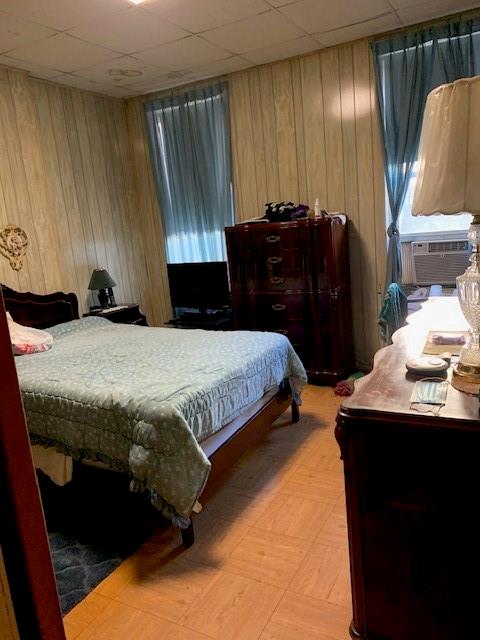 bedroom with cooling unit, a drop ceiling, and wood walls