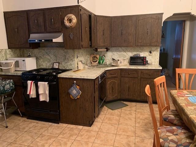 kitchen featuring tasteful backsplash, light tile patterned floors, dark brown cabinets, and black appliances