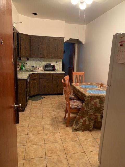 kitchen with white fridge, dark brown cabinets, light tile patterned floors, and backsplash