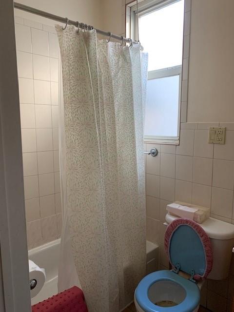 bathroom featuring tile walls, toilet, and shower / bath combo with shower curtain