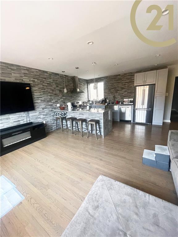 kitchen with stainless steel appliances, wall chimney range hood, dark stone countertops, white cabinets, and light hardwood / wood-style floors