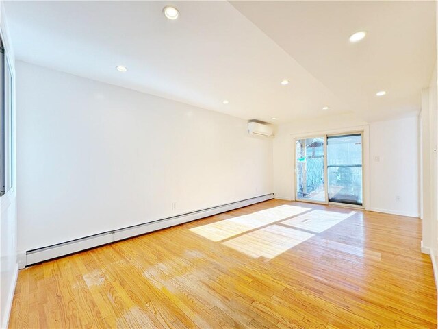 spare room featuring light wood-type flooring, a wall mounted air conditioner, and a baseboard heating unit