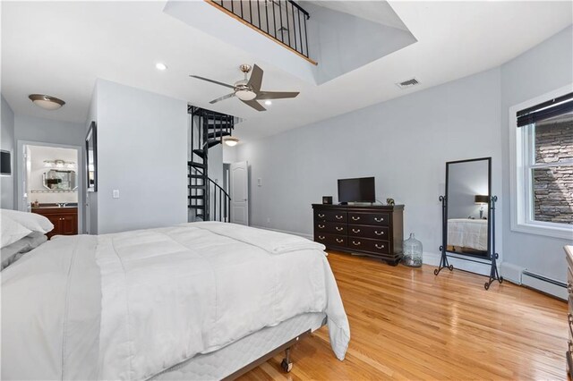 bedroom with a raised ceiling, ensuite bathroom, light hardwood / wood-style flooring, and ceiling fan