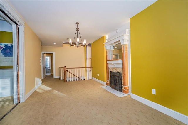 unfurnished living room featuring an inviting chandelier, carpet, baseboards, and a fireplace with flush hearth