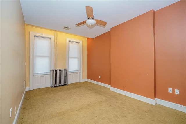 spare room featuring light carpet, visible vents, baseboards, radiator heating unit, and ceiling fan