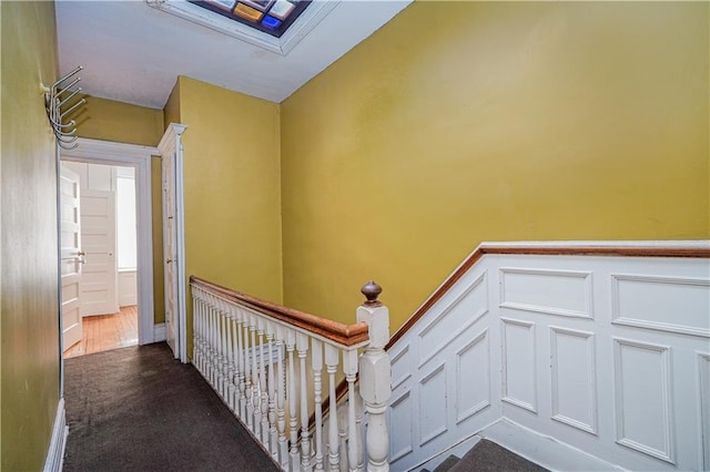 hallway featuring wainscoting, carpet flooring, and a decorative wall