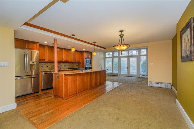 kitchen featuring stainless steel appliances, french doors, light carpet, hanging light fixtures, and a kitchen island with sink