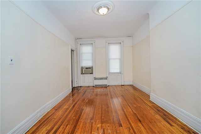 unfurnished room featuring radiator heating unit, cooling unit, hardwood / wood-style flooring, and baseboards