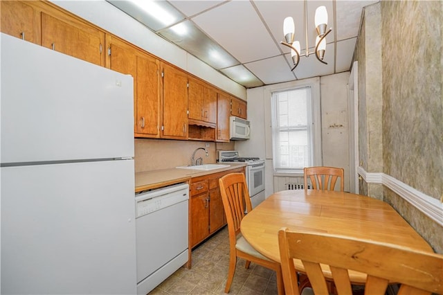 kitchen featuring a chandelier, white appliances, a sink, light countertops, and brown cabinetry