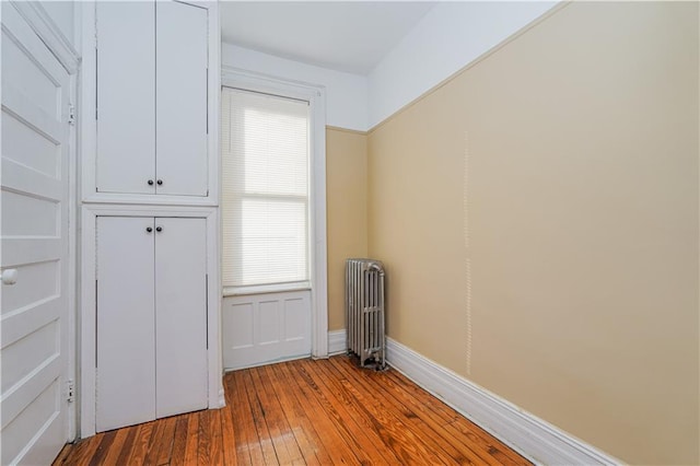 empty room with wood-type flooring, baseboards, and radiator heating unit