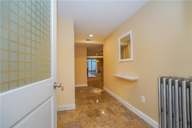 hall featuring radiator heating unit, visible vents, and baseboards