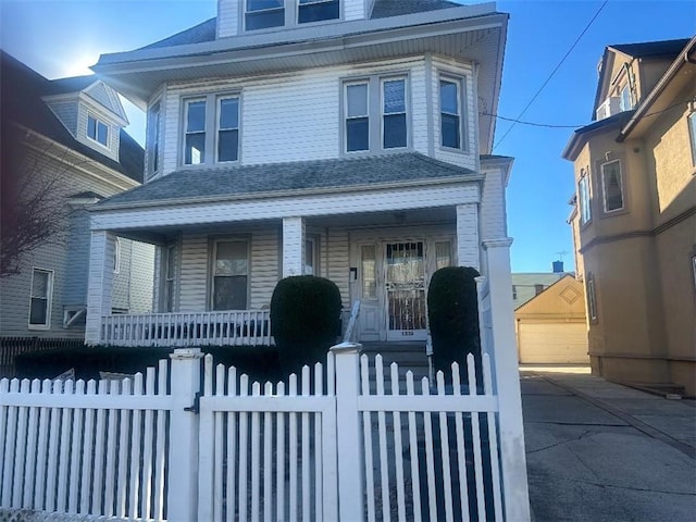 american foursquare style home with a fenced front yard, a porch, a shingled roof, and an outdoor structure