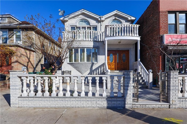 view of front of property featuring a balcony, brick siding, and a fenced front yard