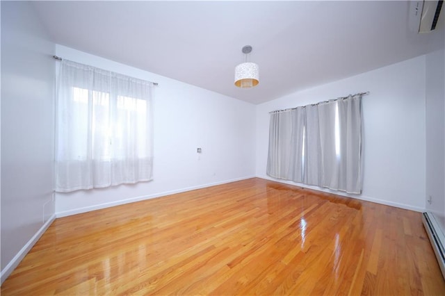 empty room featuring baseboards, a baseboard heating unit, a wall unit AC, and wood finished floors