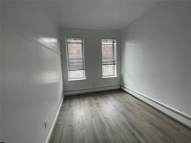 unfurnished room featuring hardwood / wood-style floors and a baseboard heating unit