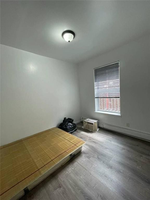 unfurnished bedroom with wood-type flooring and a baseboard heating unit