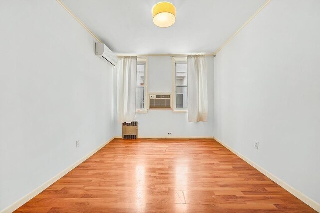 empty room with radiator heating unit, a wall mounted air conditioner, cooling unit, crown molding, and light wood-type flooring