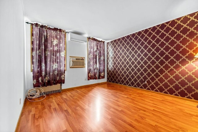 unfurnished room featuring a wall unit AC, wood finished floors, baseboards, wallpapered walls, and an AC wall unit