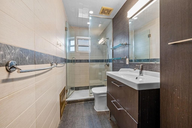 bathroom featuring vanity, toilet, a shower with shower door, and tile walls