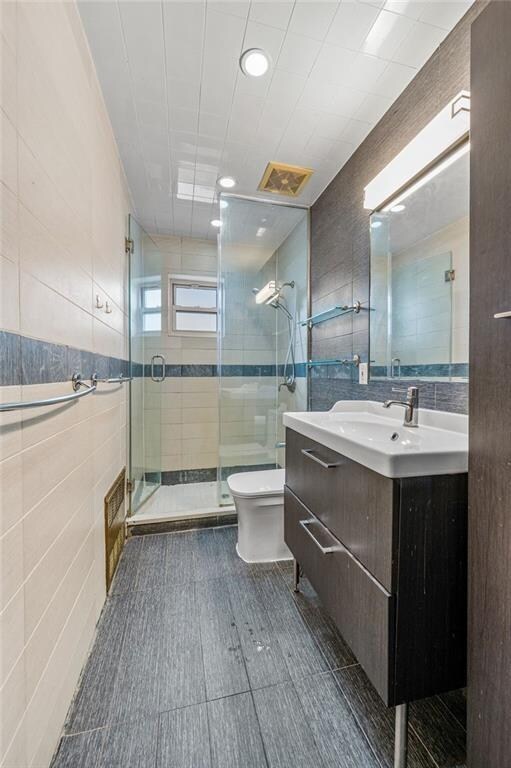 bathroom featuring walk in shower, vanity, toilet, and tile walls