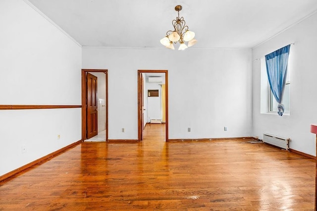 empty room featuring a notable chandelier, wood finished floors, crown molding, and a baseboard radiator