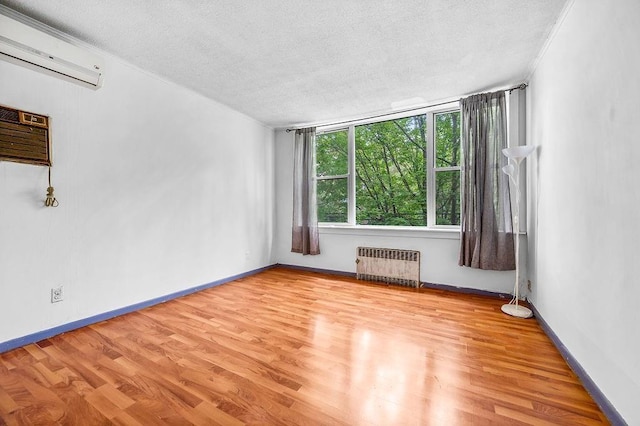 empty room featuring a textured ceiling, a wall mounted air conditioner, radiator heating unit, and wood finished floors