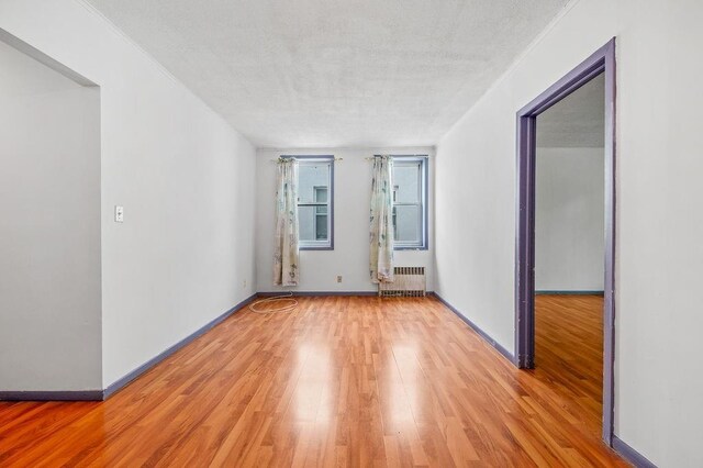 empty room with radiator, a textured ceiling, and light wood-type flooring