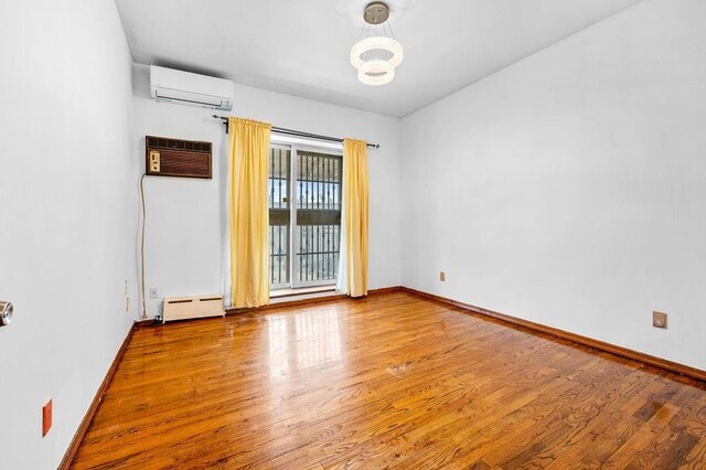 empty room featuring hardwood / wood-style flooring, a wall unit AC, and baseboard heating