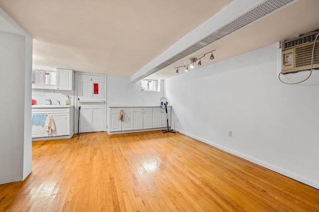 interior space featuring light wood-style flooring, baseboards, a wall mounted air conditioner, and a sink