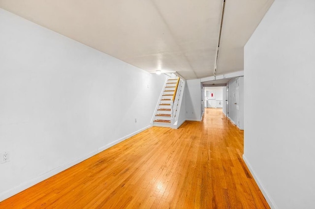 basement featuring baseboards, light wood-style flooring, and stairs