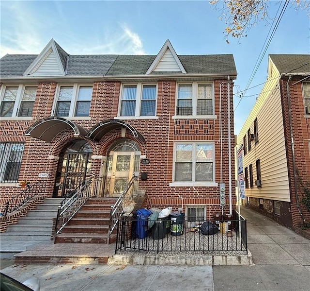 townhome / multi-family property with a fenced front yard, brick siding, and roof with shingles