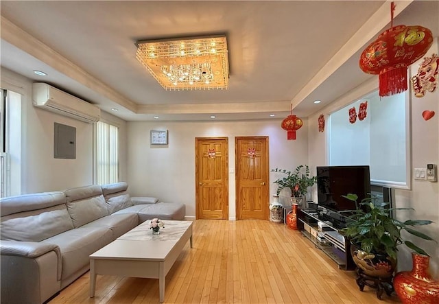 living room featuring a tray ceiling, light wood finished floors, a wall unit AC, and electric panel