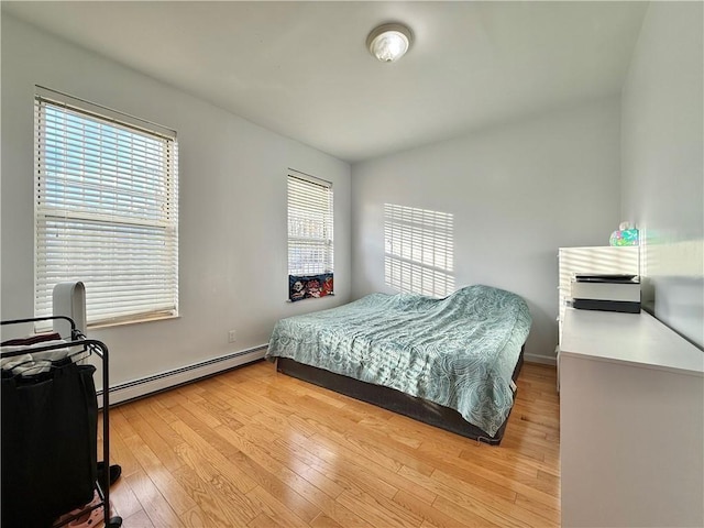 bedroom featuring a baseboard heating unit, light wood finished floors, and baseboards