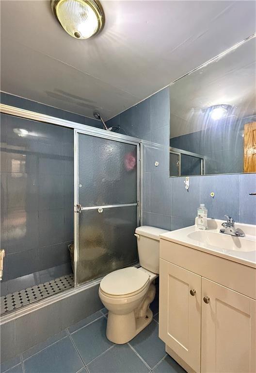 bathroom featuring tile patterned flooring, tile walls, a shower stall, and vanity