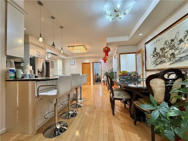 kitchen with white cabinets, a breakfast bar area, pendant lighting, light wood-type flooring, and stainless steel refrigerator with ice dispenser