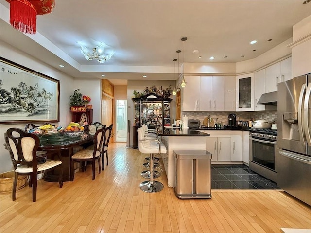 kitchen with a breakfast bar, stainless steel appliances, dark countertops, white cabinetry, and under cabinet range hood