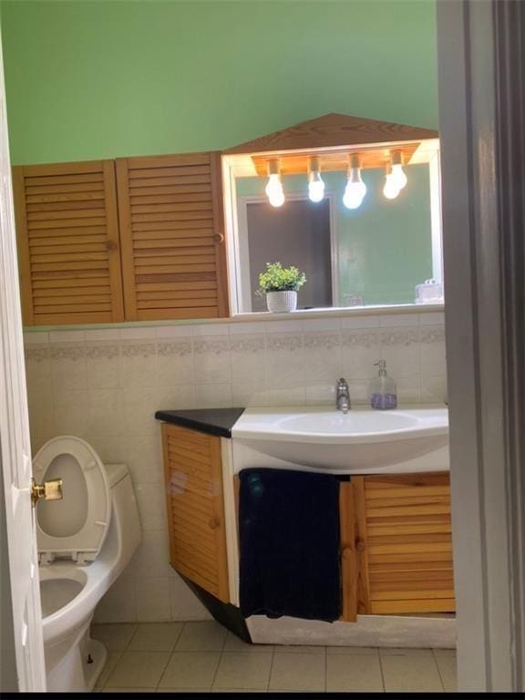 bathroom with toilet, vanity, tile patterned floors, and tile walls