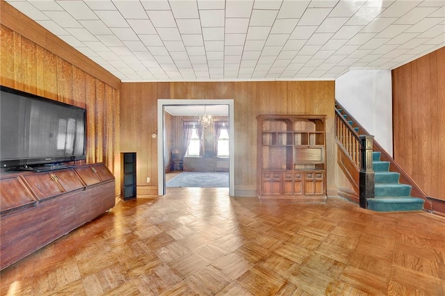 living room featuring an inviting chandelier, wooden walls, and light parquet floors