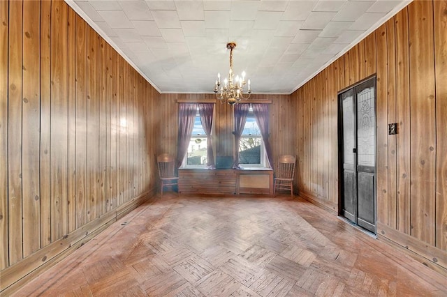 spare room with an inviting chandelier, wooden walls, parquet floors, and crown molding