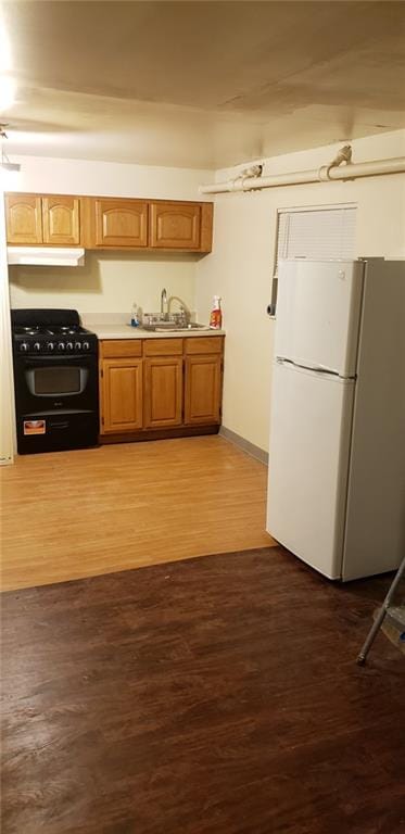 kitchen featuring sink, hardwood / wood-style flooring, black gas range oven, and white fridge