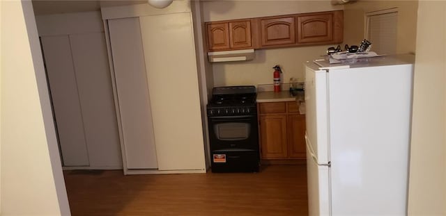 kitchen with light wood-type flooring, black gas stove, and white fridge