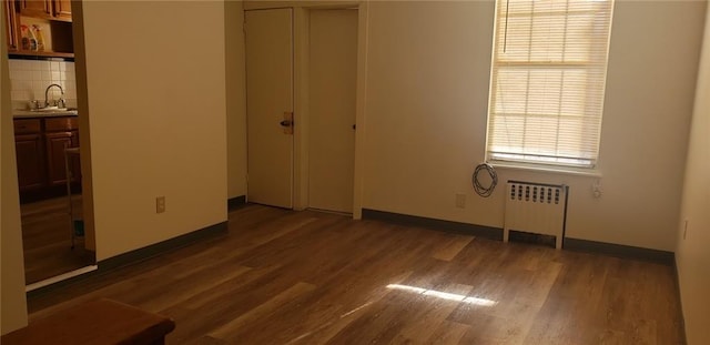 unfurnished bedroom featuring dark wood-type flooring, sink, radiator heating unit, and a closet