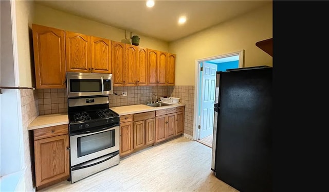 kitchen featuring stainless steel appliances, brown cabinetry, light countertops, and a sink