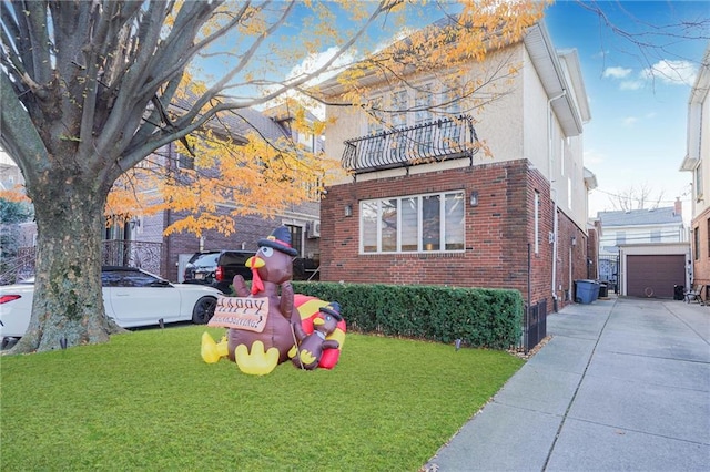 view of front facade with a front yard, a balcony, stucco siding, an outdoor structure, and brick siding