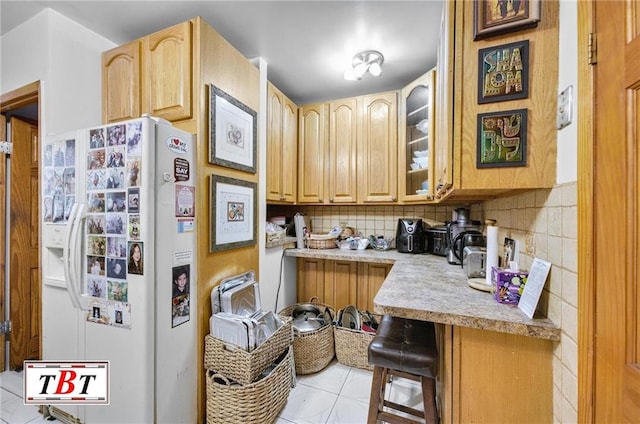 kitchen with light brown cabinetry, decorative backsplash, a breakfast bar area, and white fridge with ice dispenser